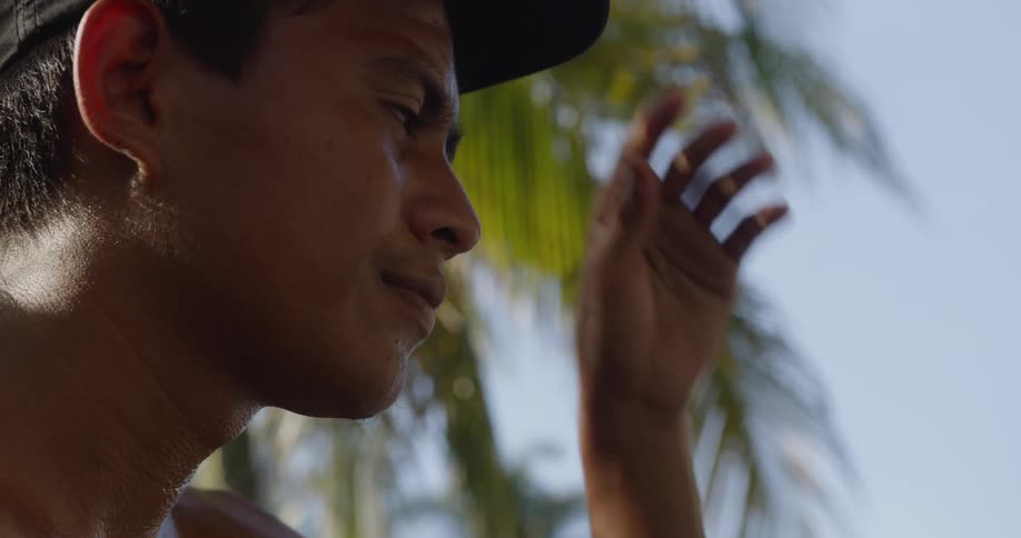A shirtless man standing outdoors adjusting a ball cap on his head