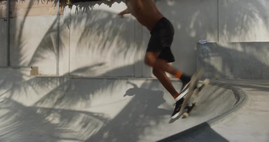 A topless skateboarder oles onto the top of a ramp before dropping in again on a sunny day