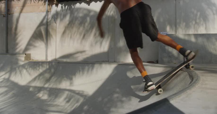 A shirtless young man on a skateboard performs a small jump on the edge of a concrete pool at a skate park