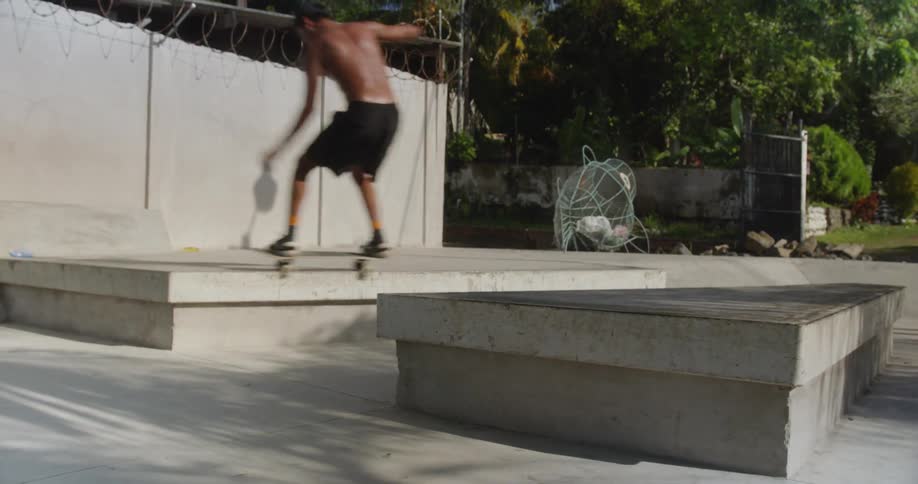 A shirtless man jumps over a platform at a skatepark on a sunny day