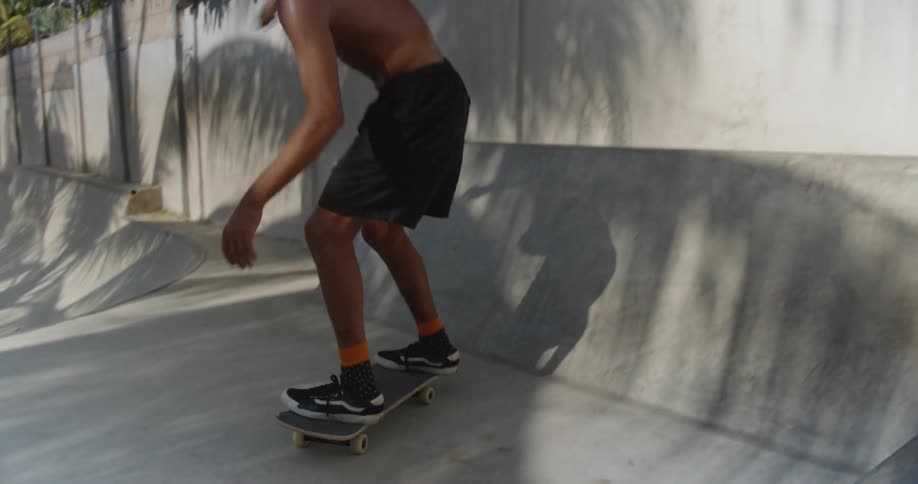 A shirtless boy rides a skateboard in a cement skate park and tries a jump