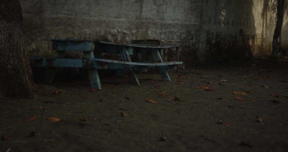 A dilapidated old picnic table sits in the dirt in front of a stone wall