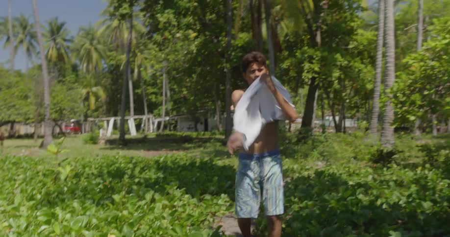 A young man puts on a t shirt as hes walking a dirt path
