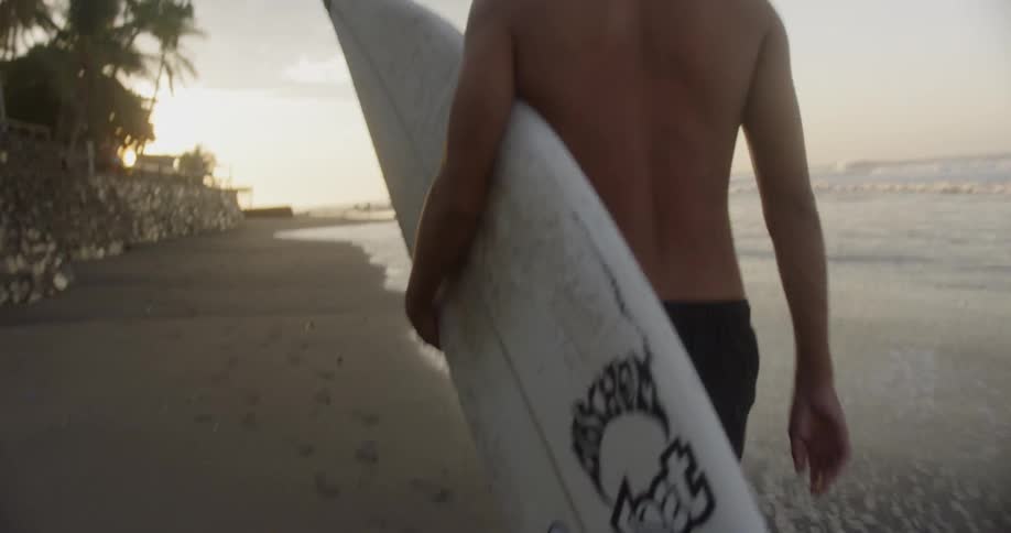 A man holds a surfboard and walks across the coast