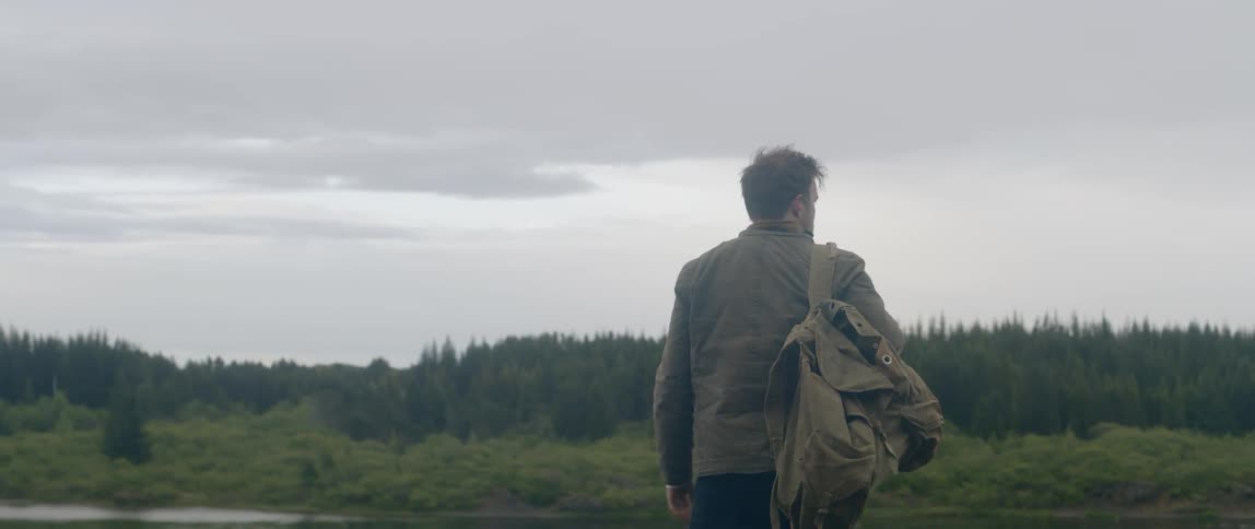 Man wearing backpack walks and looks around in the forest on a cloudy day