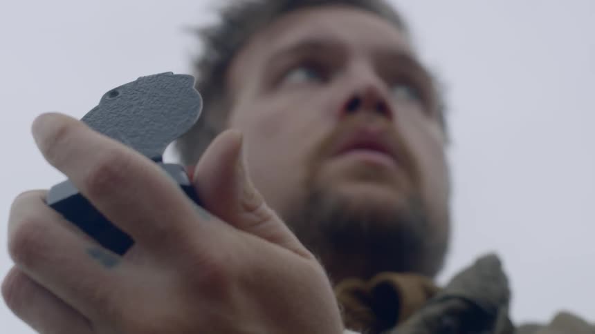 A breaded man standing outside is holding a compass as he look around from side to side