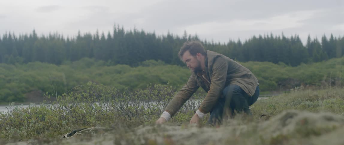 A caucasian male rolling out a tent on grass