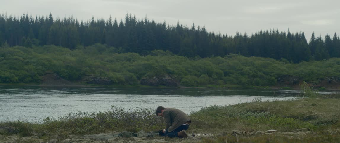 A man kneels on the ground near a flowing river