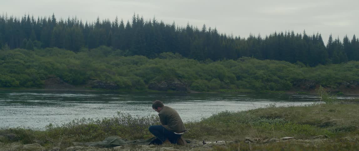 A man sets up a tent on the shore of a river