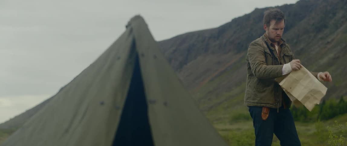 A man standing outside of a homemade tent folding up a map