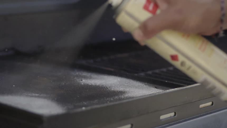 An aerosol can of cleaner is sprayed onto a grill