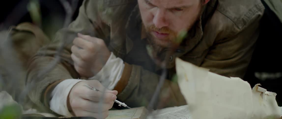 A man with a brown leather jacket looking at a book and using a compass on a map