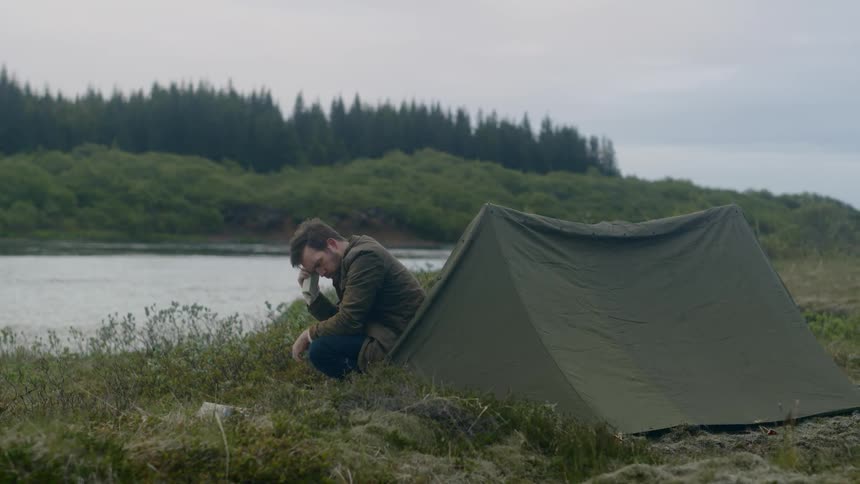 Man checks satellite phone while crouching next to tent