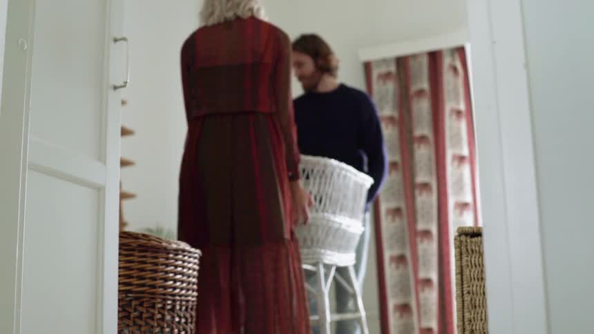 Man and woman carry a white bassinet into a room