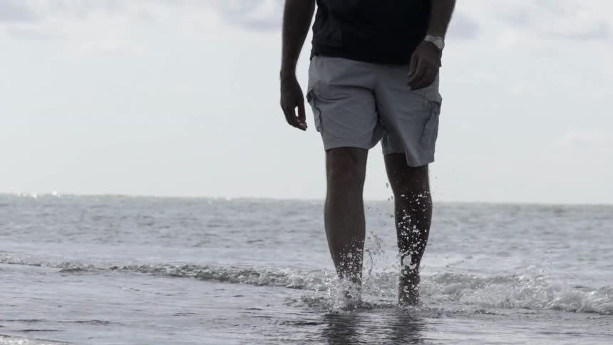 Man Wading in Ocean Water on Cloudy Day With Calm Coastal Atmosphere.
