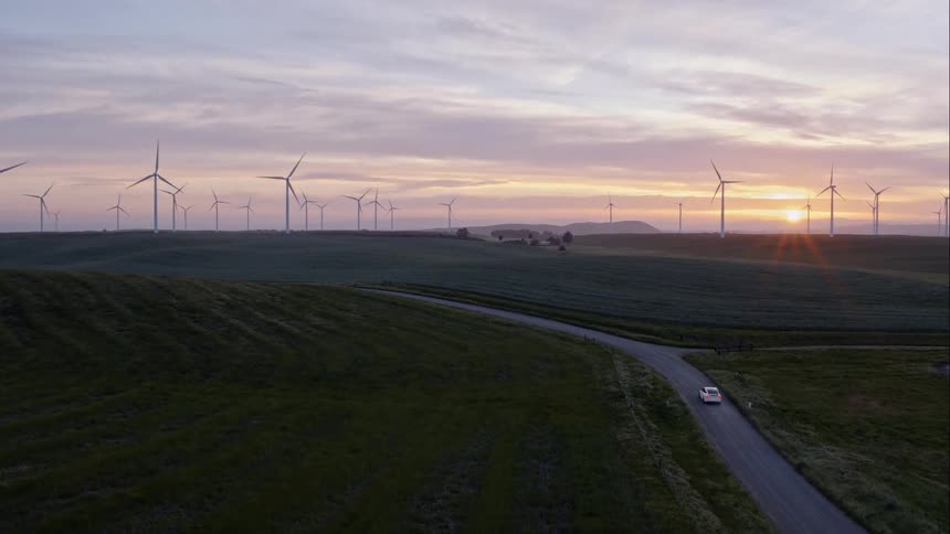 A car drives along a road beside a wind farm