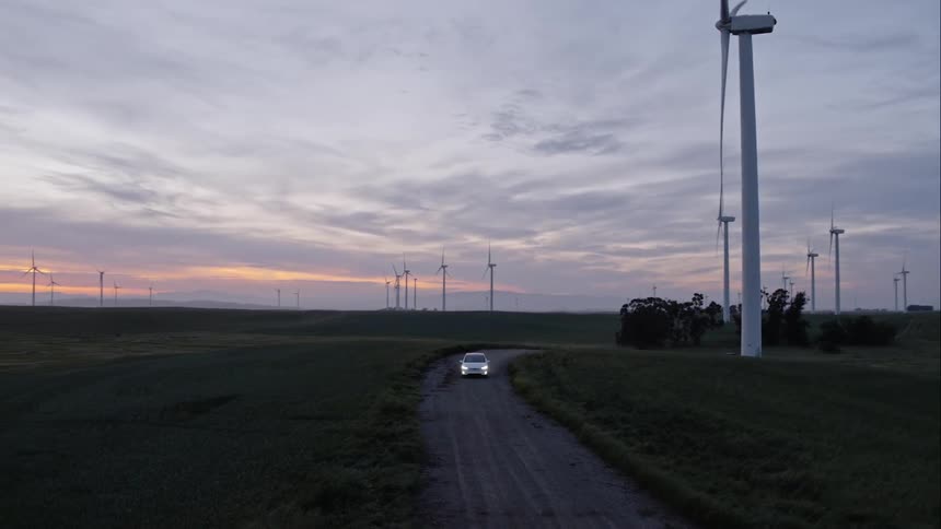 A car drives on a small road past windmills