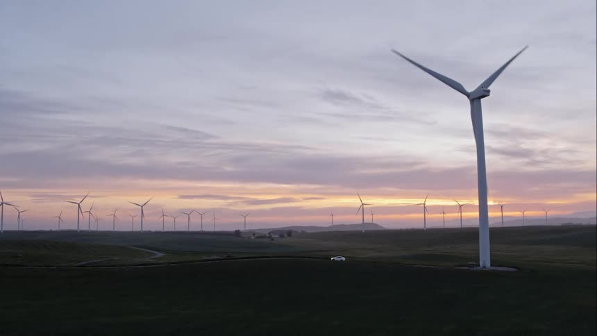 As a wind turbine rotates a car drives away from it