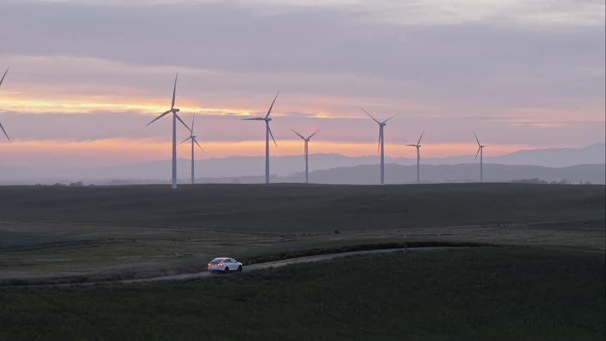 A can drives along a deserted road past wind turbines