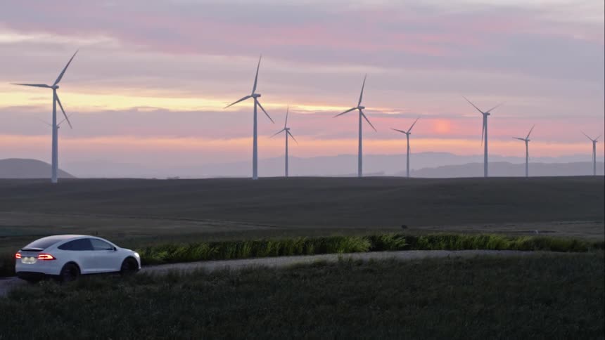 A car driving down a road surrounded by greenery and large wind turbines