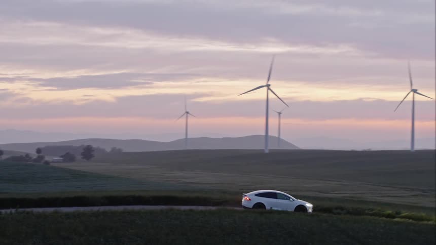 A car is parked by a wind mill farm and then drives