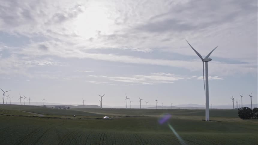 A truck travel on a dirt road through fields and a wind farm