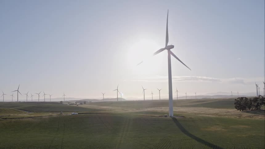 Wind turbine blades turn as a car approaches on a dirt road
