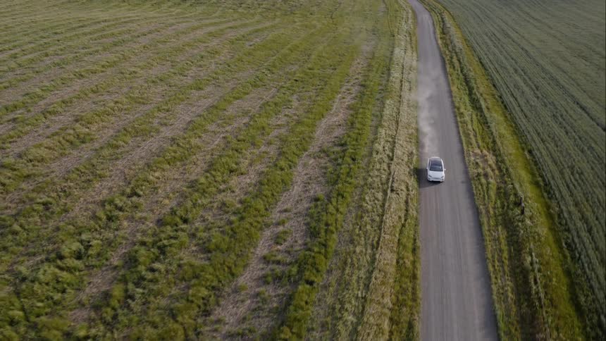 A white car driving on the road with a wind farm in the background