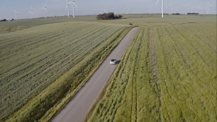 Car driving on a road through a field near a windmill farm during the day
