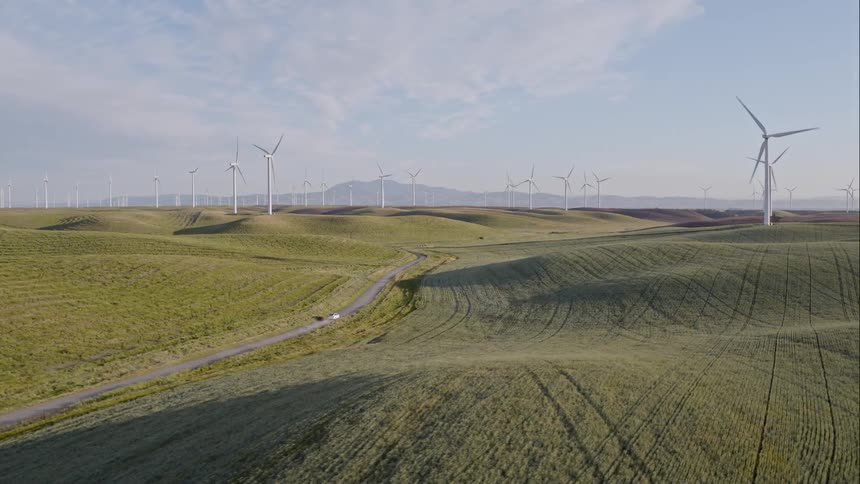 An aerial view of a car driving on a rural road near a wind farm