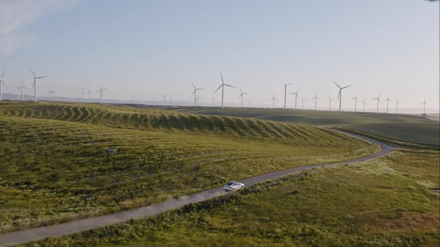 White car driving through a wind farm on a dirt road
