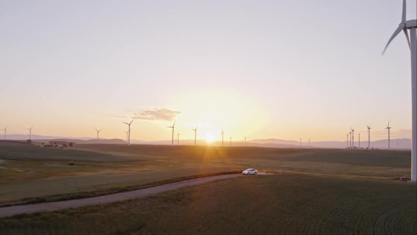 Wind turbine spins as a car travels down the road