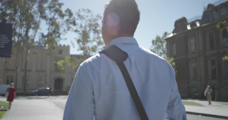 Male student wearing a blue shirt walking through campus at a university