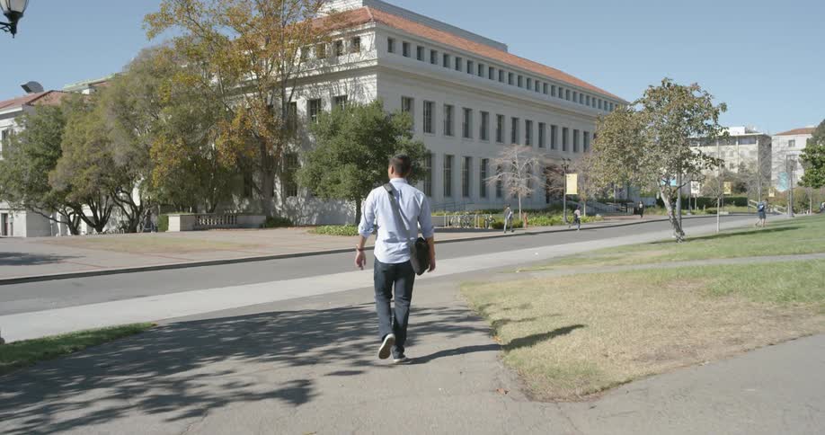 A white man wearing a satchel walks towards a building