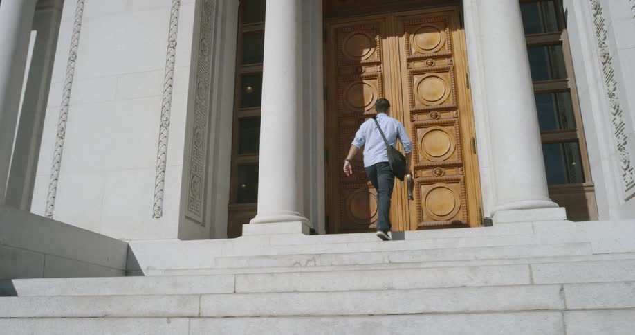 A man walks up the stairs and opens the large doors to a building