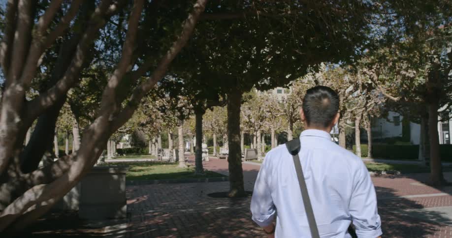A man walks down a small town sidewalk with a briefcase over his shoulder