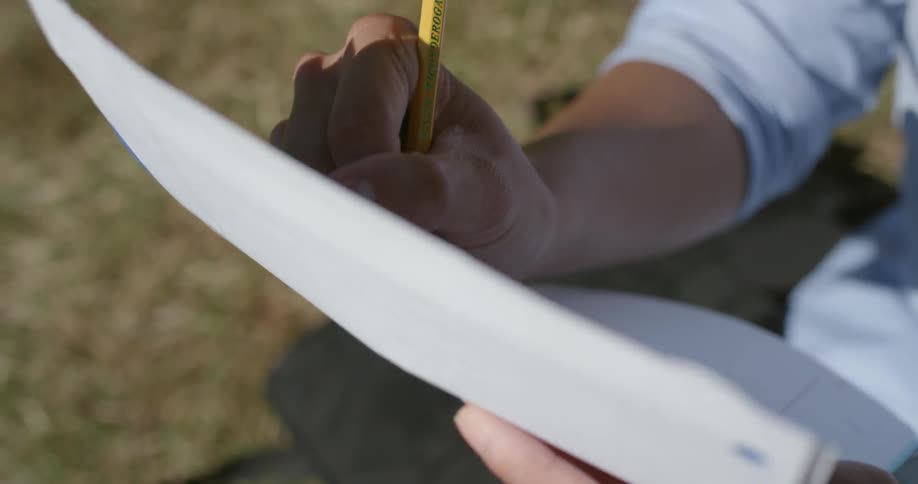 A person is writing on paper on the grass