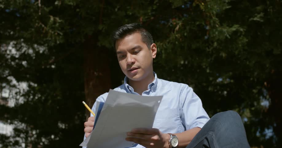 A man reads and takes notes on papers while sitting outside