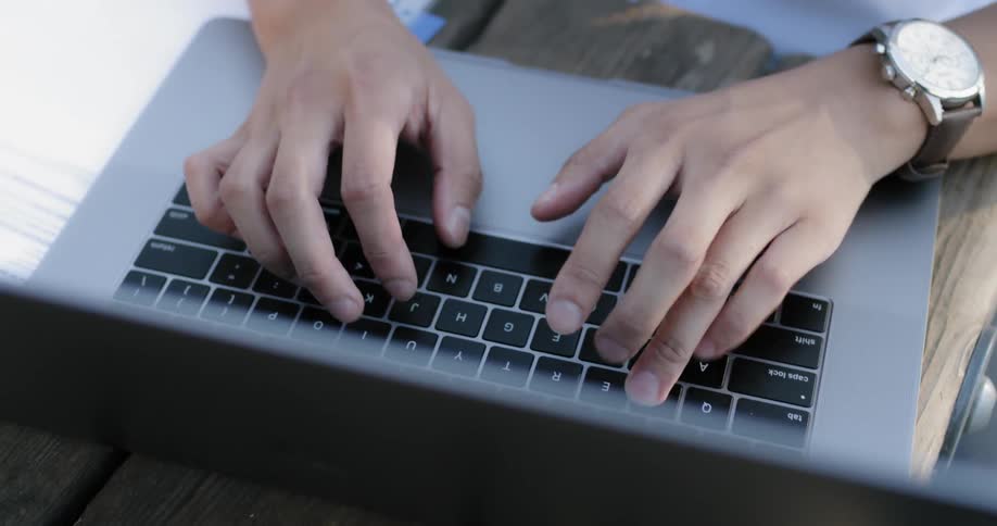 A person with a wristwatch types on a laptop