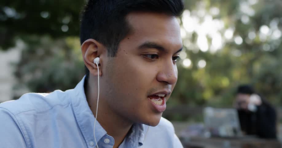 A man is talking to a laptop in a city park