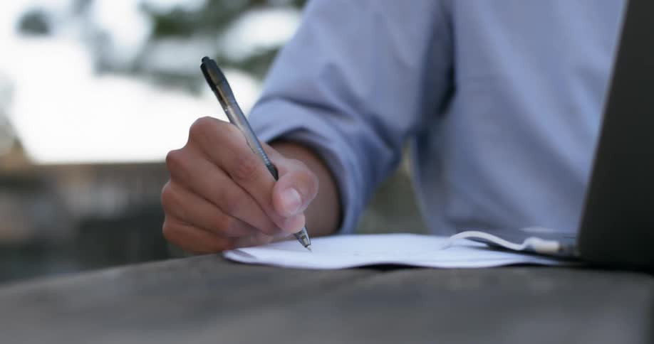 A man writing on paper next to a laptop