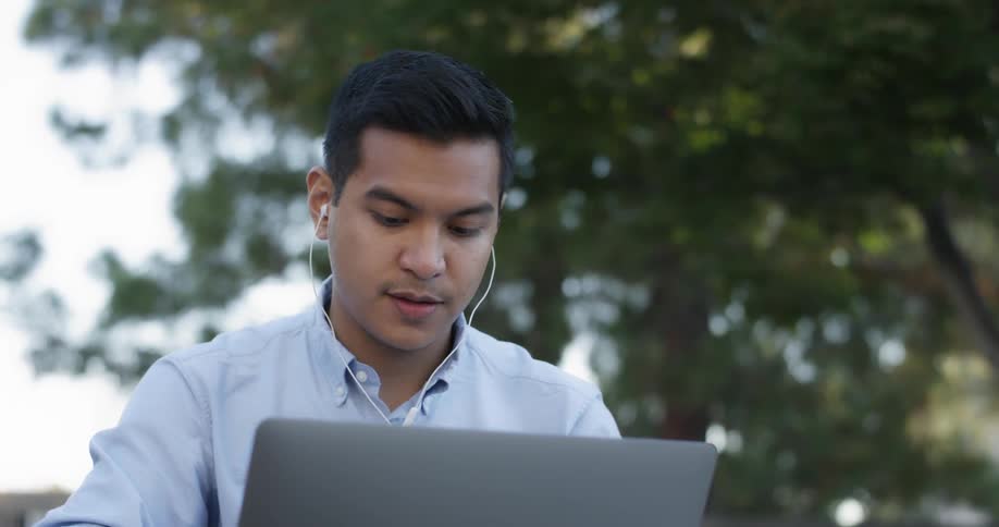 A young man is wearing earbuds while he works on his laptop