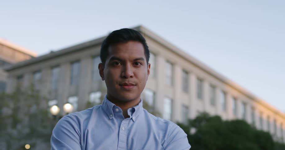 A man in a blue button up shirt stands in front of a building
