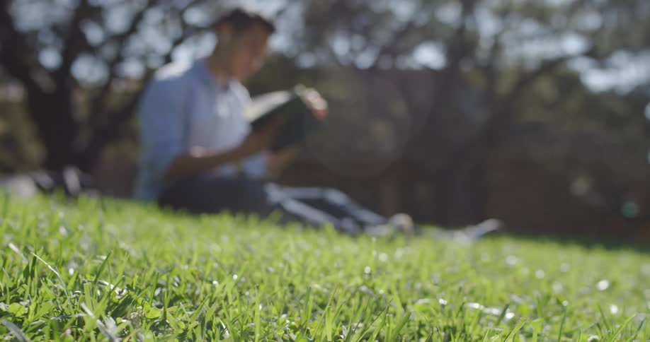 A man is reading a book outdoors while sitting down