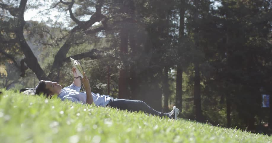 A man is laying in the grass reading a book