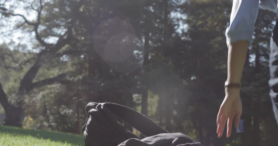 A man takes off his backpack and sits on the grass