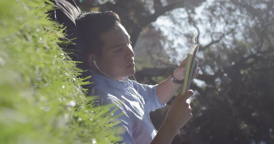 A man lays down in the grass reading a book