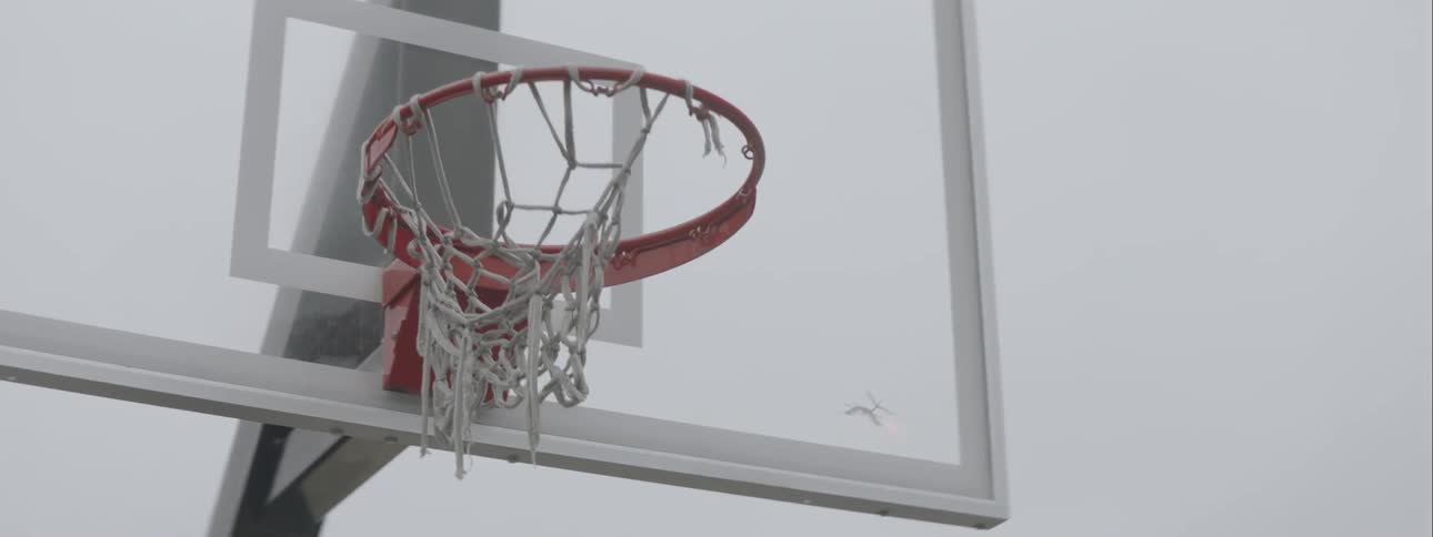 A basketball backstop with a ripped net hanging off the hoop