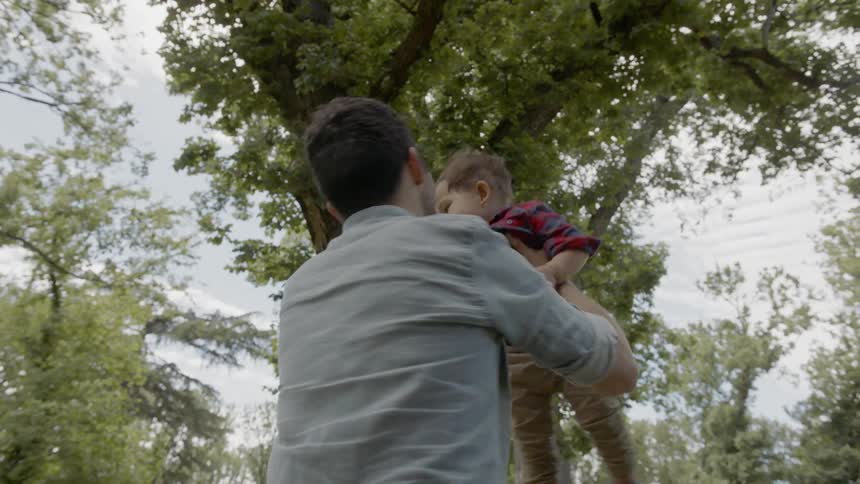 A man holds a little boy up in the air and spins in a circle