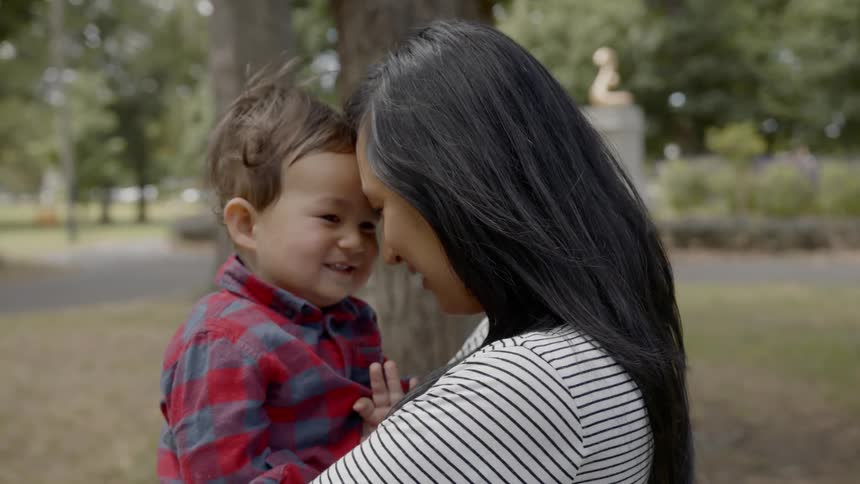 Mother cuddles kisses and plays with child outdoors